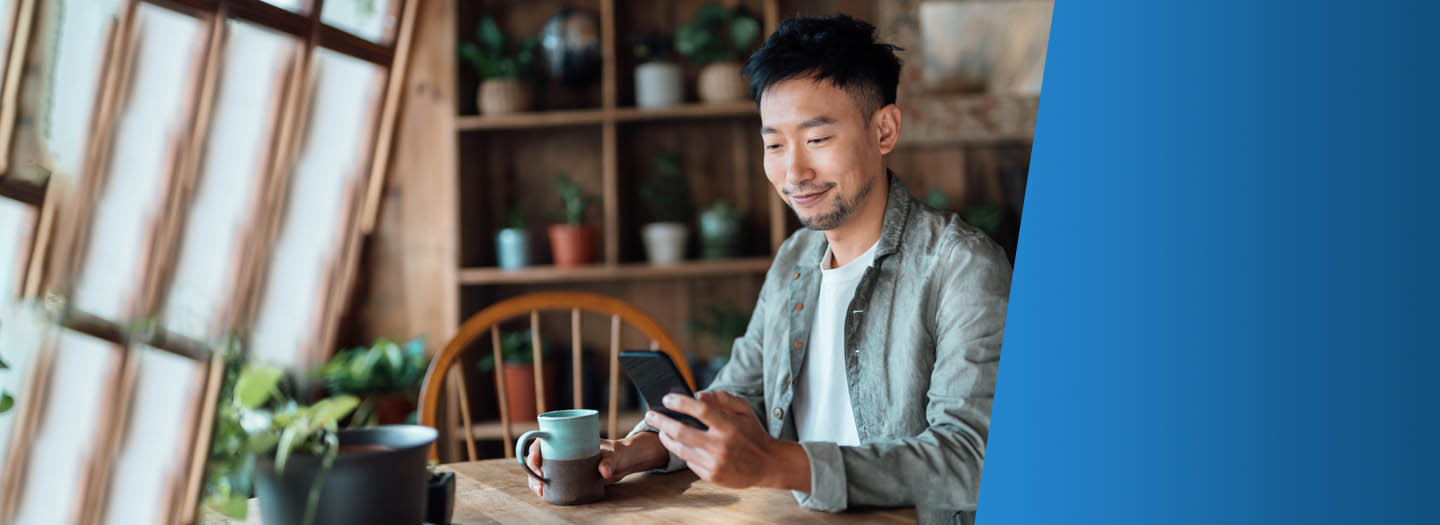 Man looking at his mobile phone and drinking coffee in his kitchen